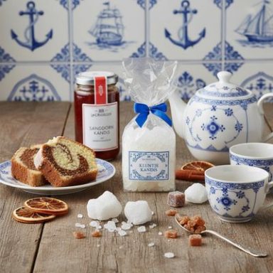 Kluntje & Kandis Tee-Service mit Marmelade, Zuckerstückchen und Kuchen auf einem Holztisch.